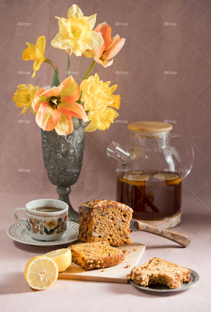 still life in vintage style with cupcake and tea or coffee for breakfast, with a bouquet of spring flowers, daffodils and tulips in a pewter vase