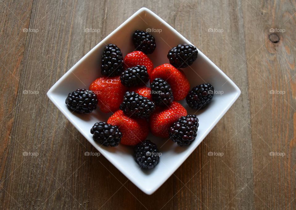 Bowl of strawberries and blackberries on wood background