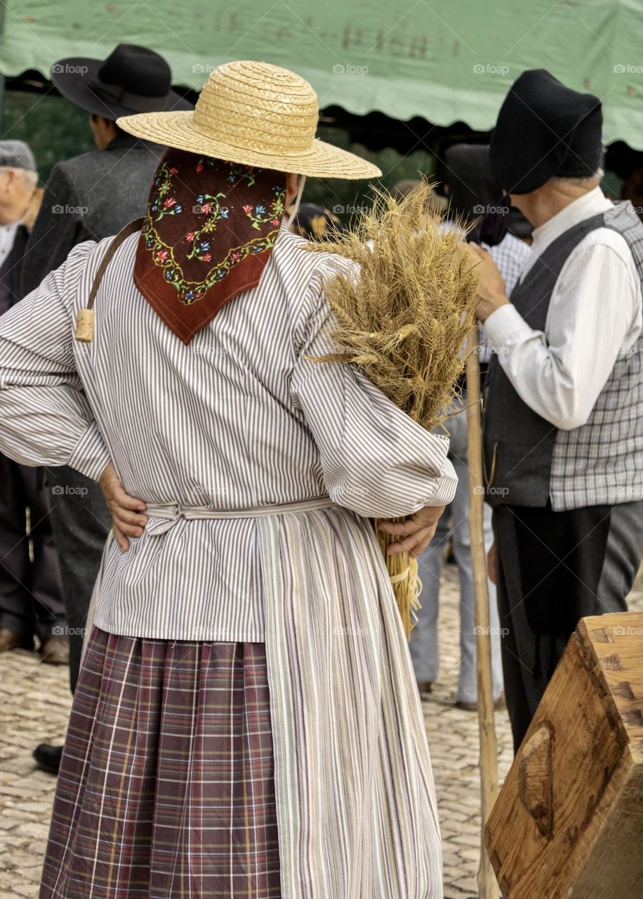 A woman in traditional, rural attire holds a sheaf of wheat at a local village festa in Central Portugal 