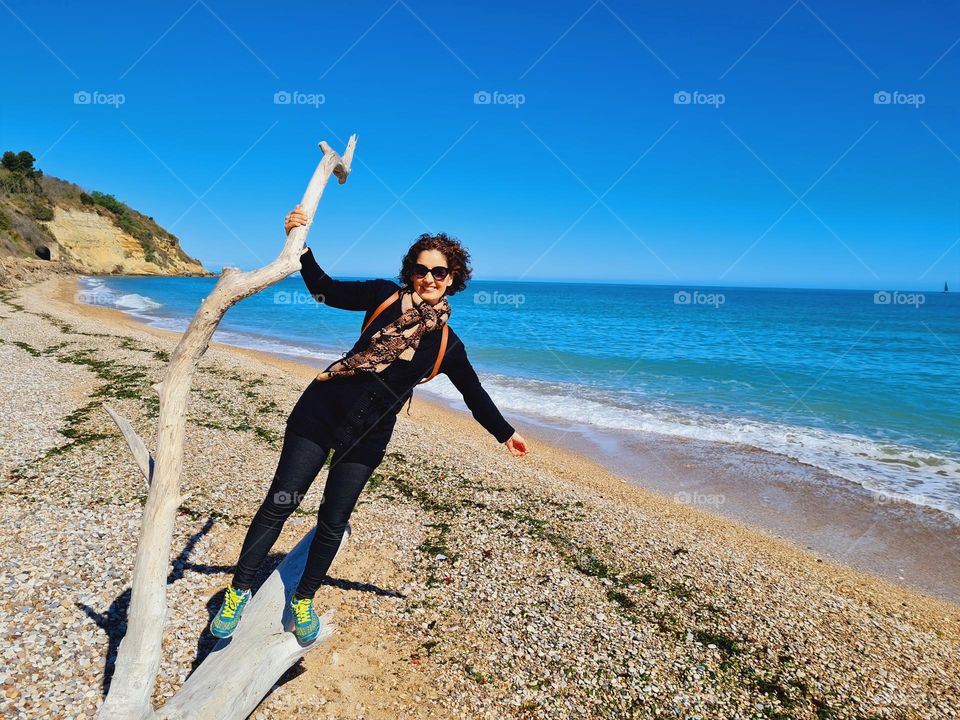 smiling woman climbs a log stranded on the beach and wears a python scarf