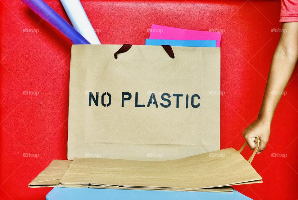 Paper bag which wrote no plastic on its top and it contains colour papers and some one holding one paper bag and drag it from among them . 