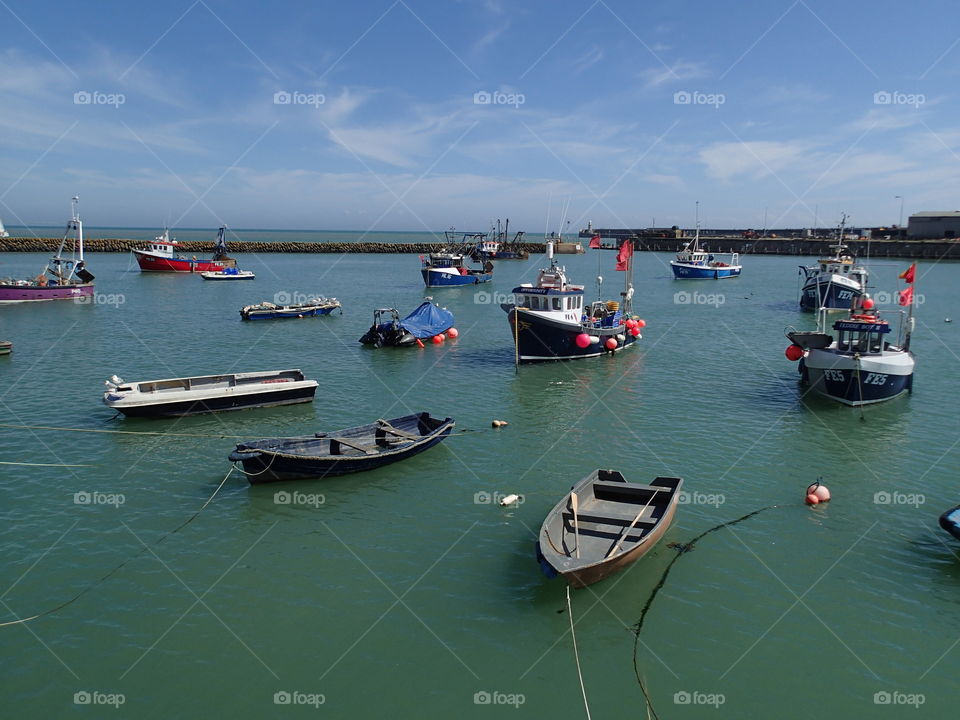 Fishing boats tied up or anchored in the calm harbor in Folkestone England on a sunny summer day. 