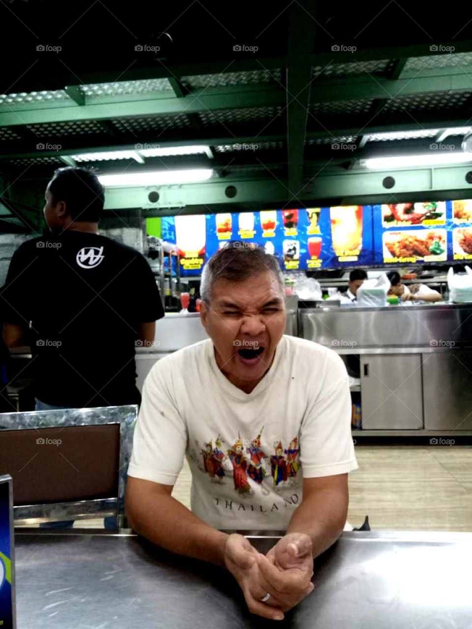 A man wearing a white t-shirt is sitting on a chair and yawning because he is sleepy