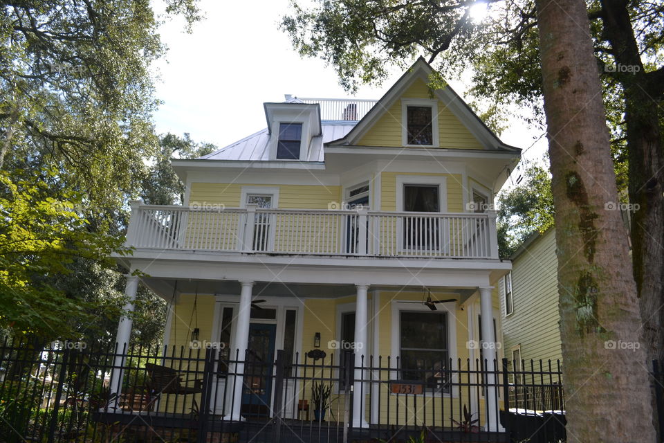 Restored historic 2-story home painted yellow with wrought iron fence in front