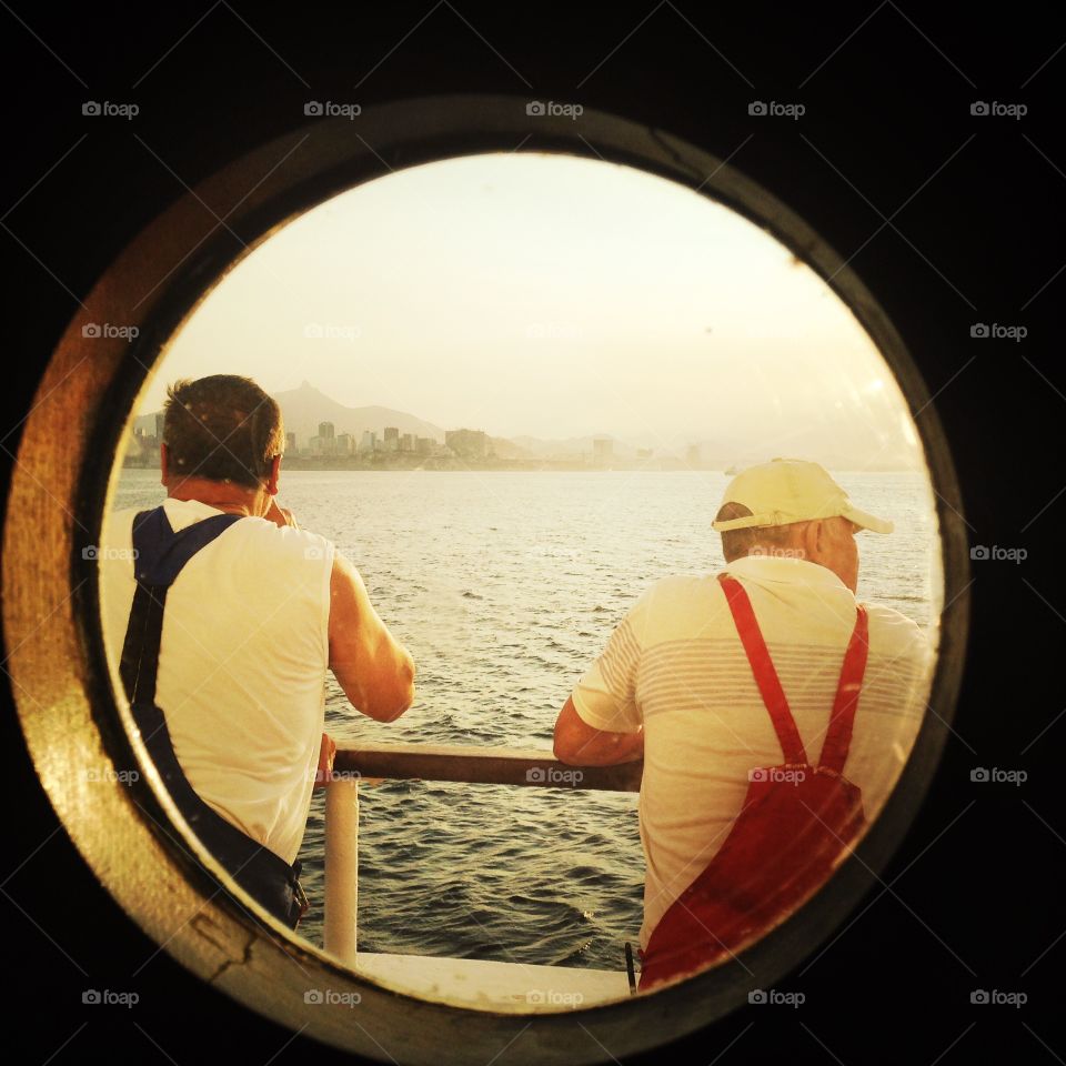 Two sailors gaze out at the port of Rio de Janeiro during sunrise.