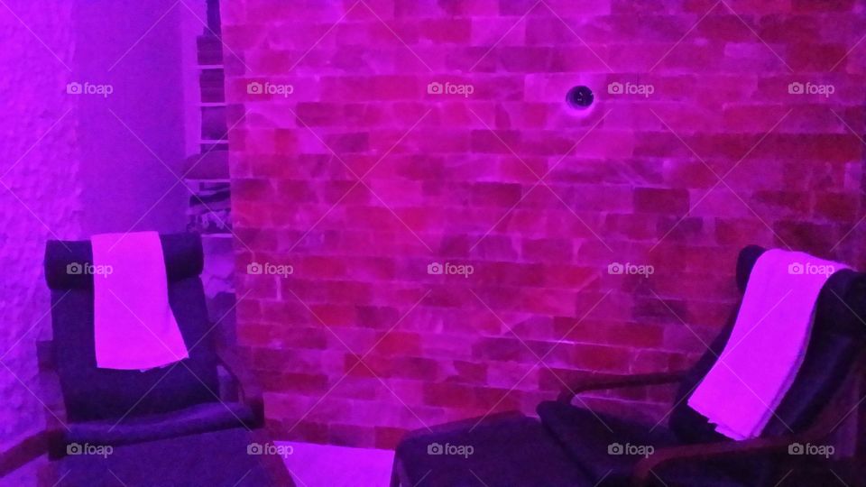 Salt room therapy; a brick wall made of salt with chairs to relaxe with colored lighting