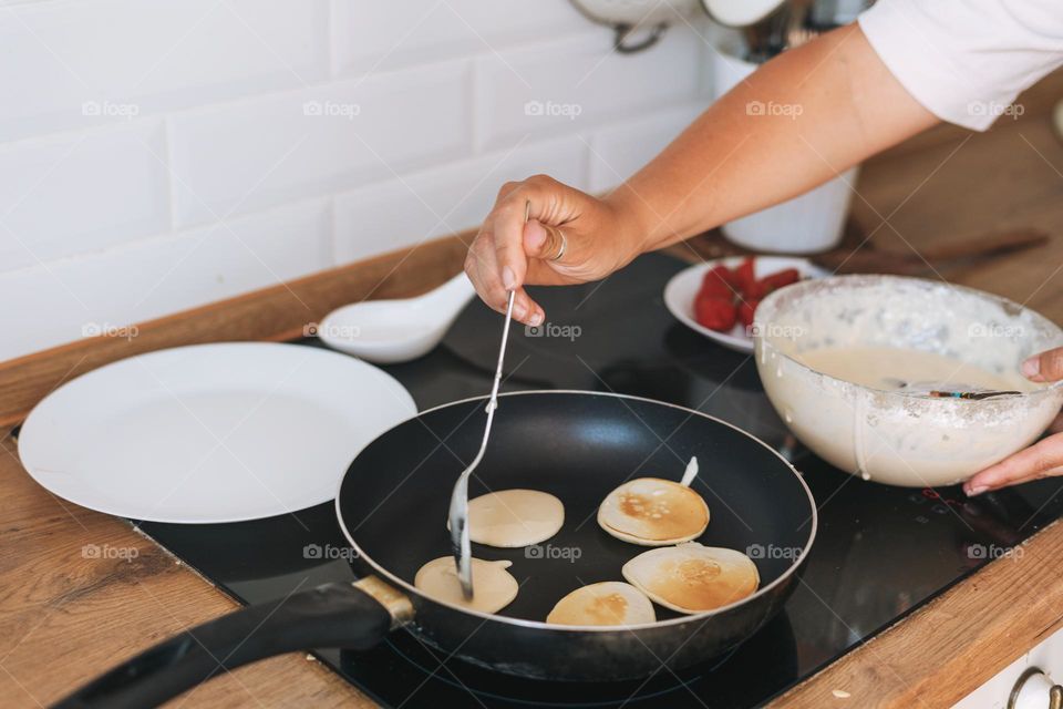 Young woman cooks pancakes in a frying pan on electric stove in the kitchen at home