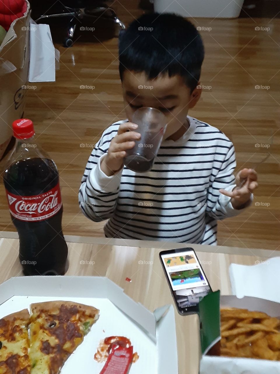 an food on his hands, a fone on his eyes and a coca cola on his mouth.