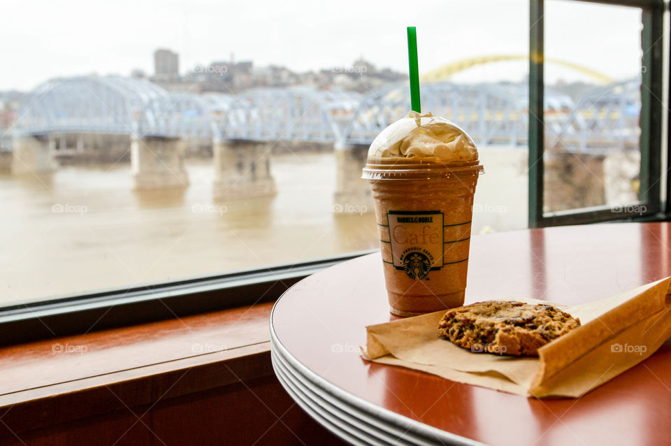 Starbucks frappachino cup and cookie on a table at a Barnes and Noble cafe with a view of a river, bridge and city in the background