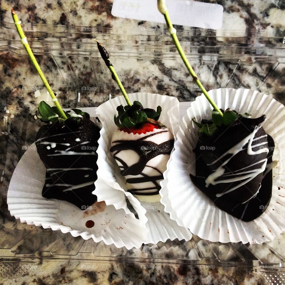 Three dark- and white-chocolate-covered strawberries with long stems nestled into their wrappers on a granite countertop