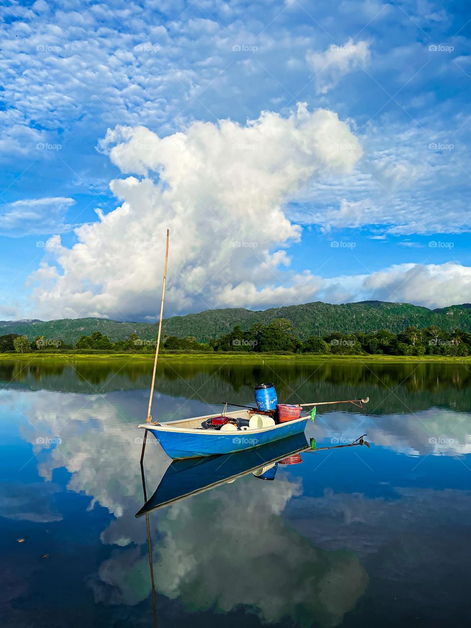 A lonely boat on a calm lake with reflection of the blue cloudy sky and far seen mountains
