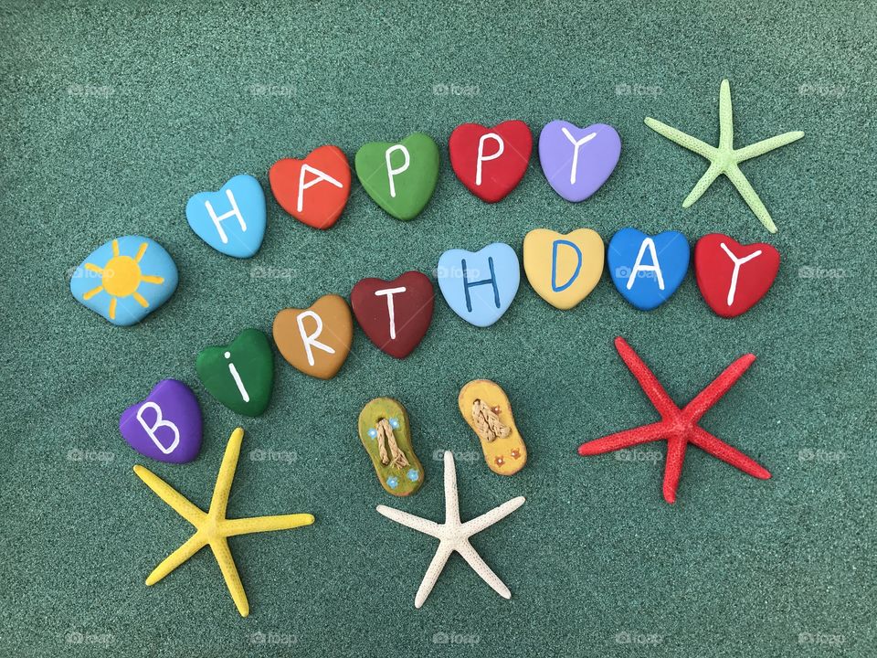 Happy Birthday message with multicolored stone hearts and starfishes over green sand 