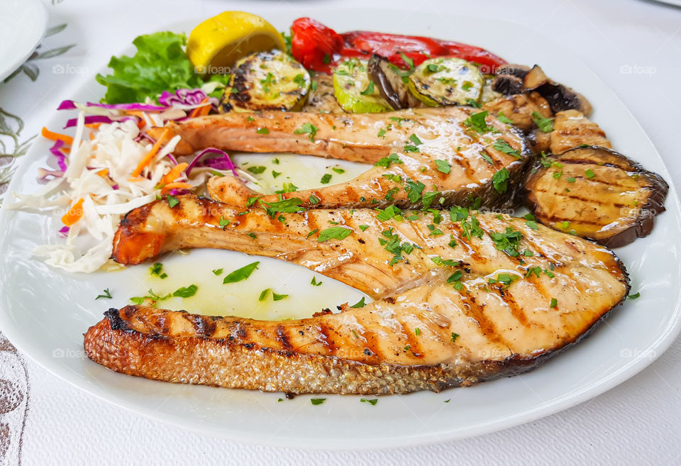 Sliced swordfish grilled with grilled vegetables like eggplant, zucchini and pepper, sprinkled with chopped parsley.