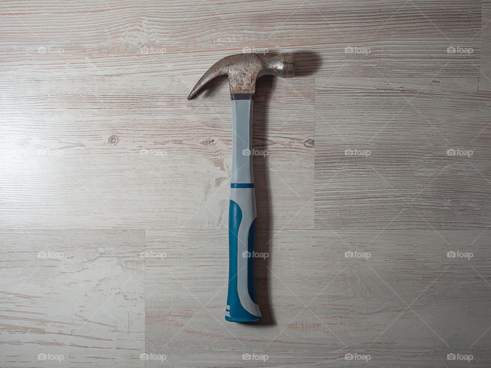 An old rusty iron construction hammer gray with blue color lies on a wooden light background