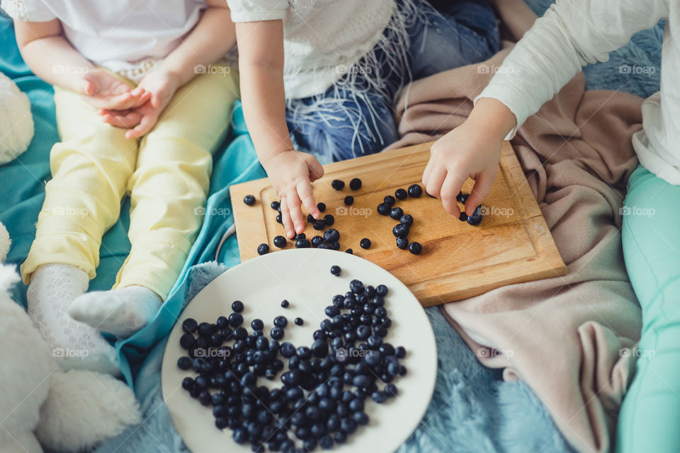 Little girls and blueberries on wood. Hands