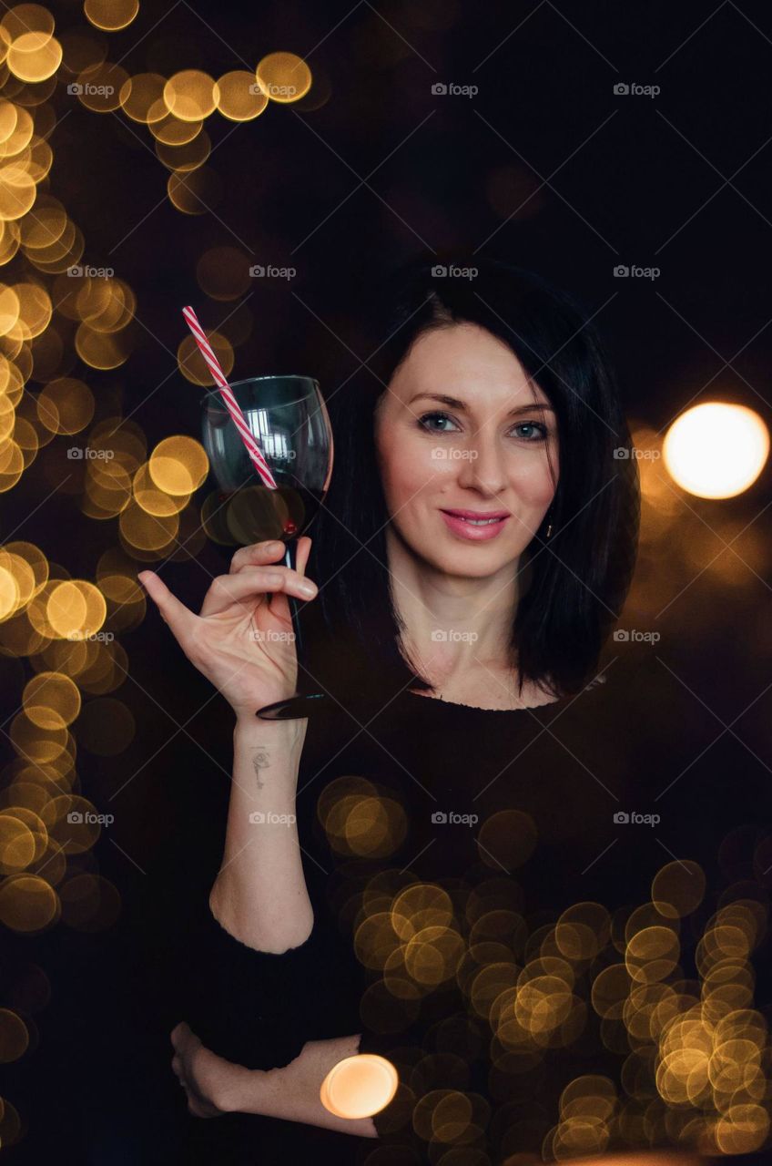 Girl with a glass of wine and a striped straw in the lights.
