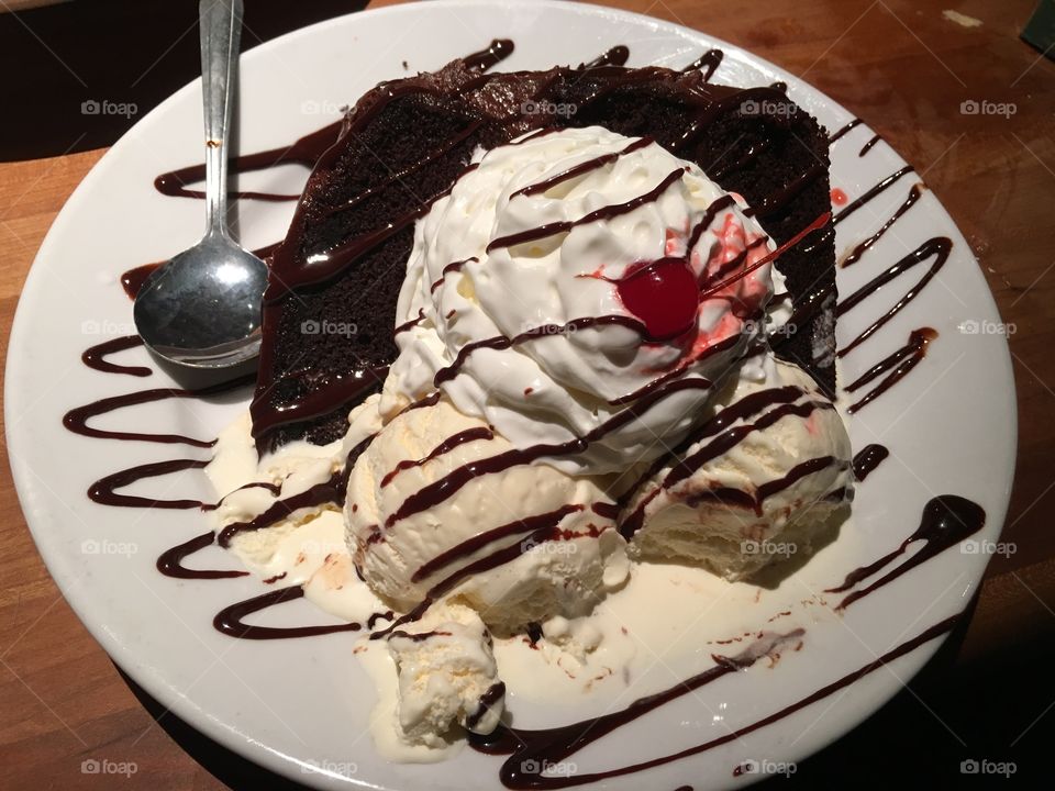 A delicious chocolate cake, topped with whipped cream, vanilla ice cream, chocolate syrup, and a cherry. 