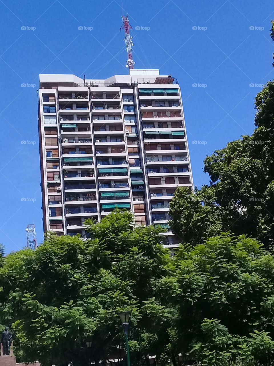 imagen de un moderno edificio de departamentos destacando entre las copas de árboles y recortado contra un cielo de verano despejado,ubicado en una céntrica avenida de la ciudad de Buenos Aires.