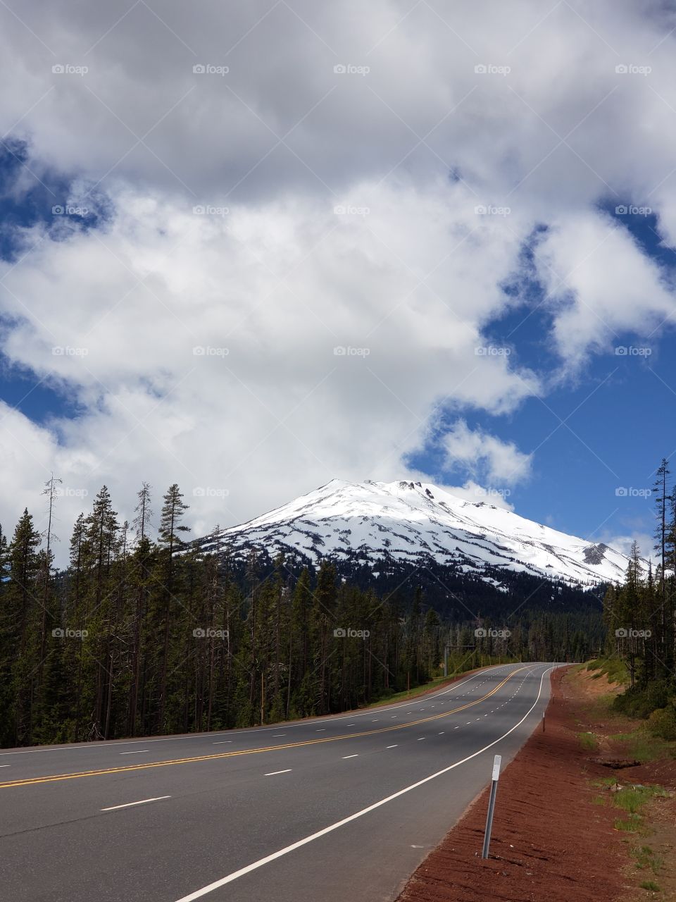 Summer road trip along Central Oregon's Cascade Lakes Highway with a view of the sun breaking through the clouds and illuminating the snow covered Mt. Bachelor.