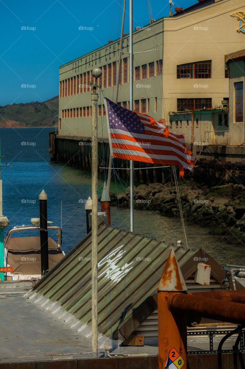 Tattered American flag flying above a dock at city yachts in San Francisco with Fort Mason in the background and the beautiful San Francisco Bay