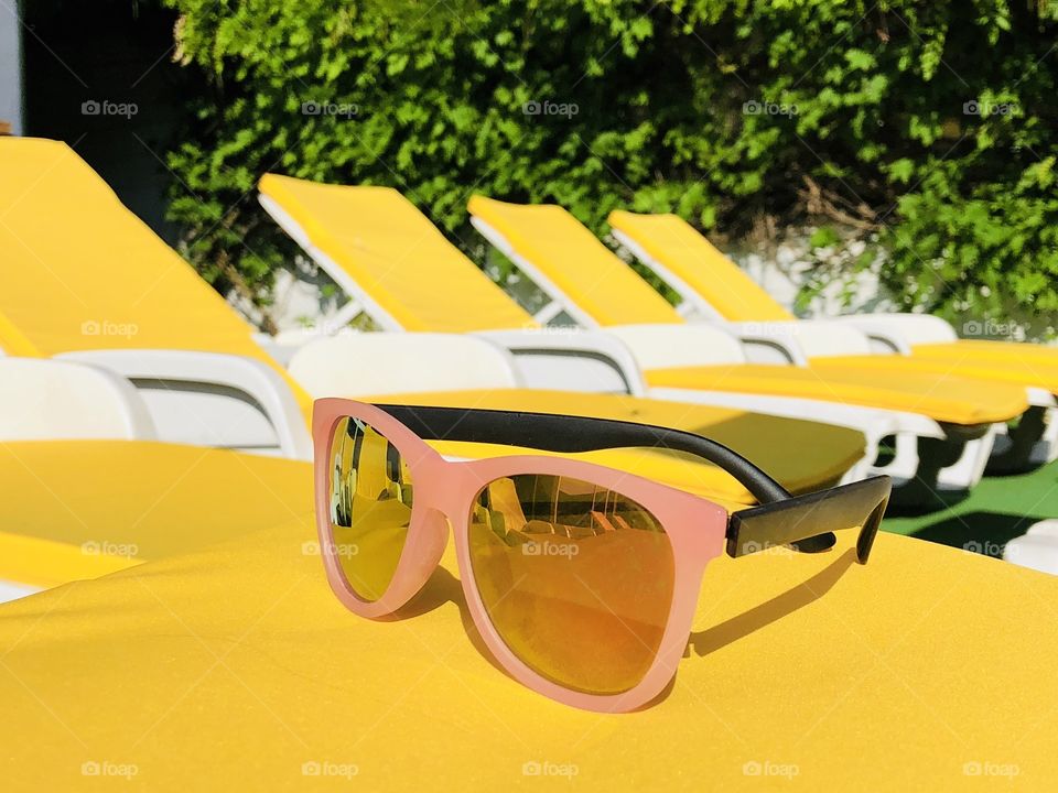 Pink sunglasses placed on a yellow sunbed with many yellow sunbeds in the background