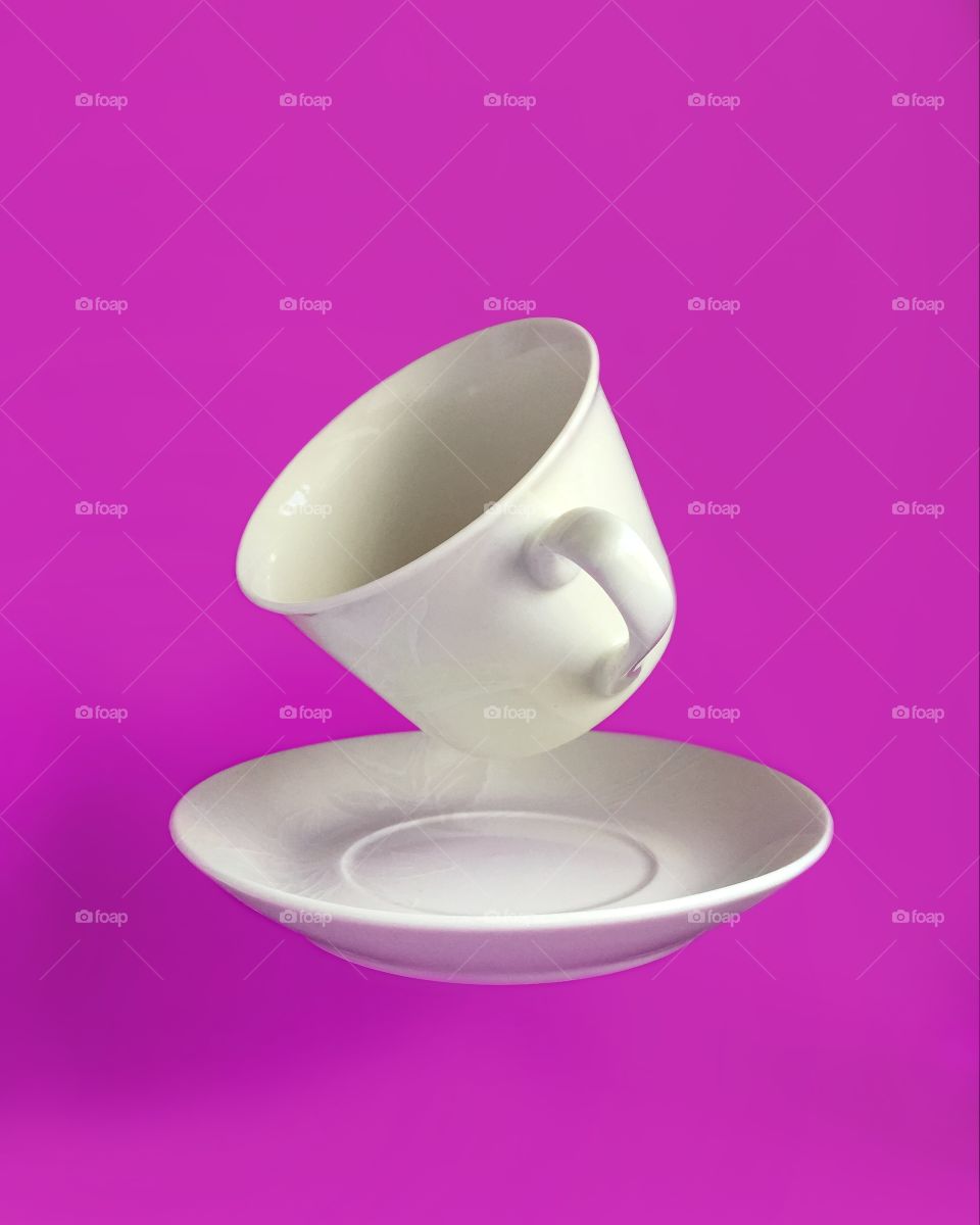 Tea cup with plate on pink background, levitation 