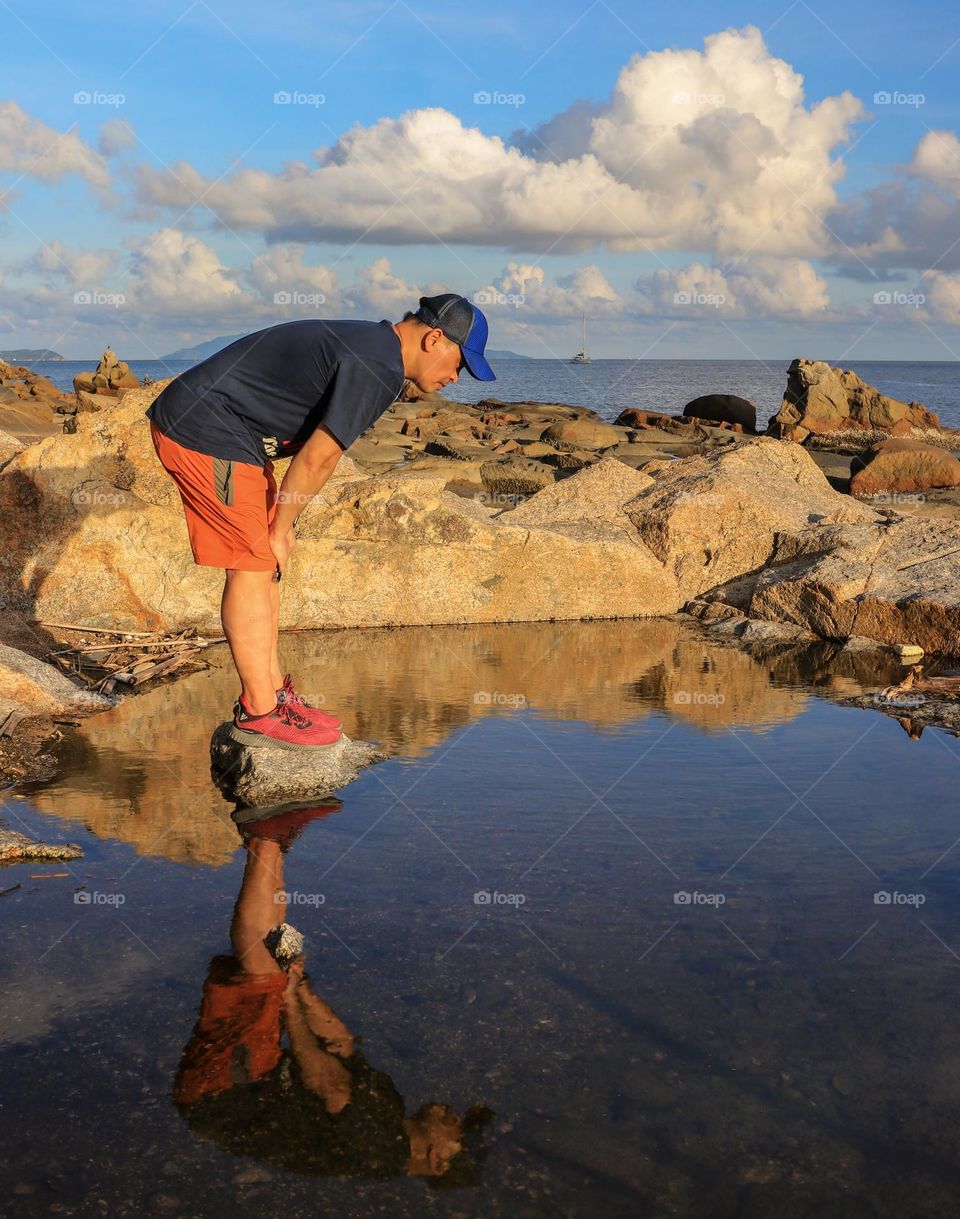 A Man on the middle of a pond standing still while observing some marine species inthe water.