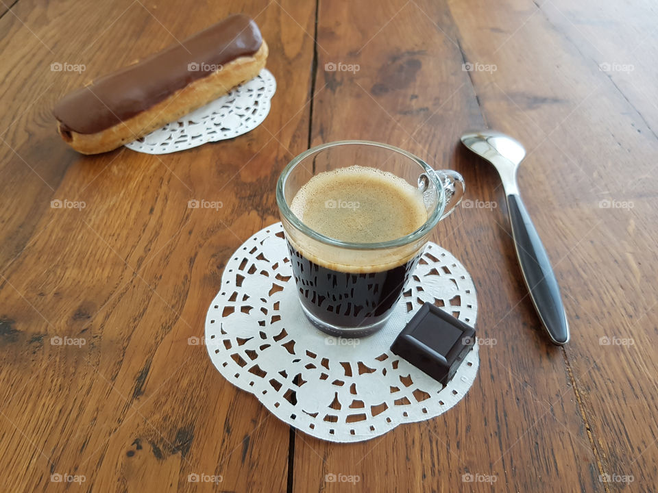chocolate treat with a cup of coffee , a square of dark chocolate and in a chocolate cake  - a chocolate eclair  - French pastry  - can be seen in the background.