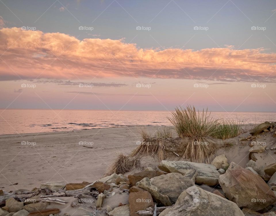 Pink and purple sunset on lake eerie shoreline on Cedar Point’s sandy, rocky beach with beach grass in foreground