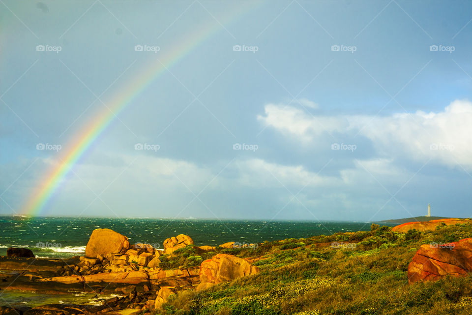 rainbow over the green ocean and rocky outcrops in the foreground with the iconic Cape Leeuwin lighthouse in the background - Augusta, Western Australia