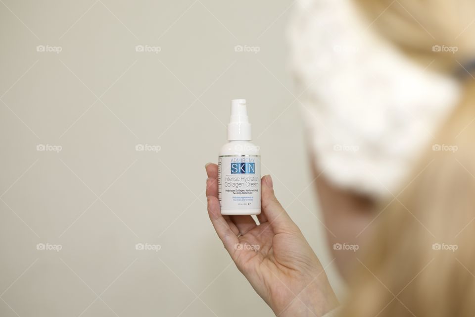 Skinecare held by woman in white headband and off white background 