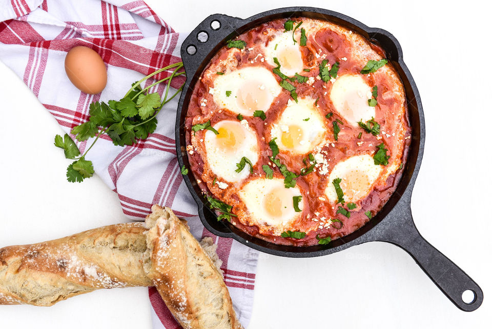 Flat lay of a shakshuka dish in a cast iron skillet with a torn baguette