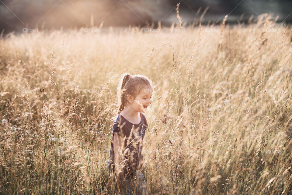 Little happy smiling girl walking through a tall grass in the countryside. Candid people, real moments, authentic situations