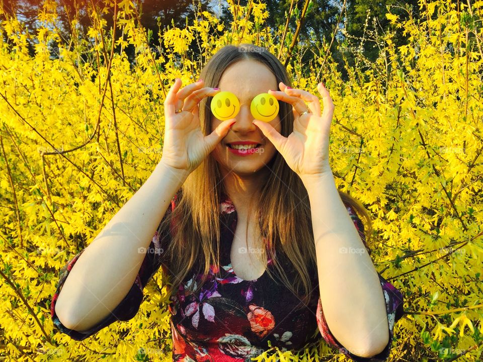 Woman holding smiley face in front of her eyes