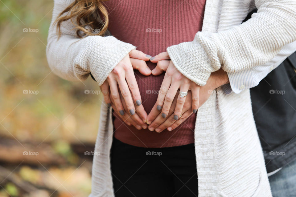 The love of a future child, parents’ hands in heart shape on pregnant belly