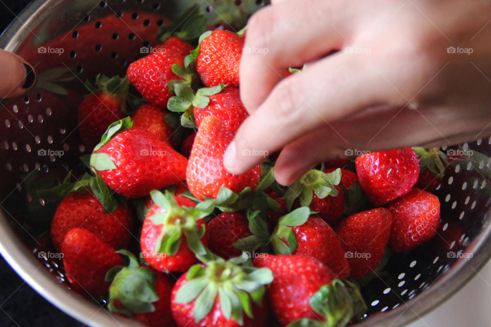 Someone getting a strawberry in a metallic bowl full of it.