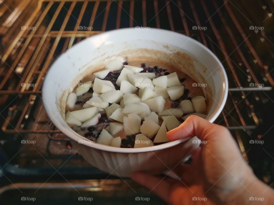 Woman's hand placing an old fashioned blueberry pear cobbler in the oven ready to cook