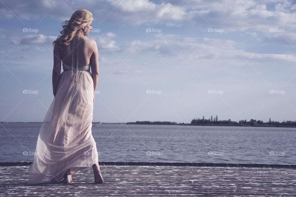 woman in beautiful dress on a wind. woman standing in beautiful peach color dress on a deck at lake