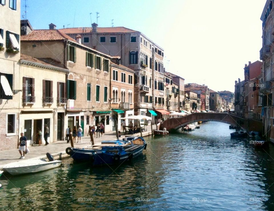 View of a canal in Venice, Italy, showing boats, bridge, buildings and reflections. 