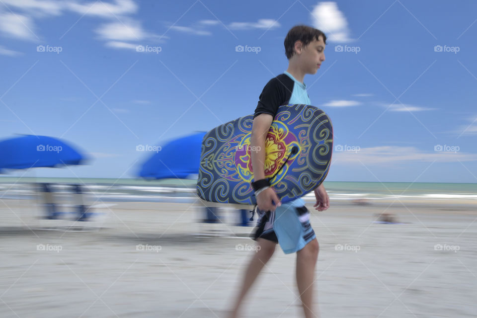 Boy walking with a Boogie Board on the beach 