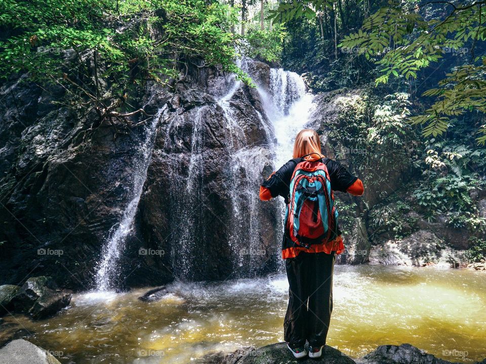 A woman standing on a rock facing a beautiful waterfall in a rainforest near Kuala Lumpur, Malaysia