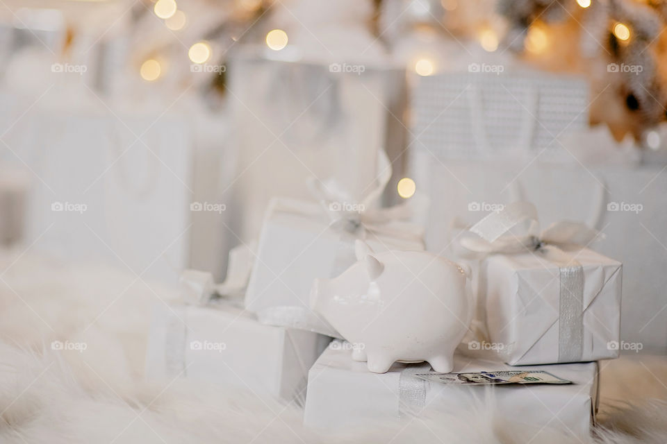 piggy bank with 100 dollars banknote in festive New Year atmosphere of scenery.  Magical bokeh with Christmas tree and bright lights.