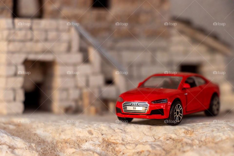 Toy red car in front yard of model of stone house