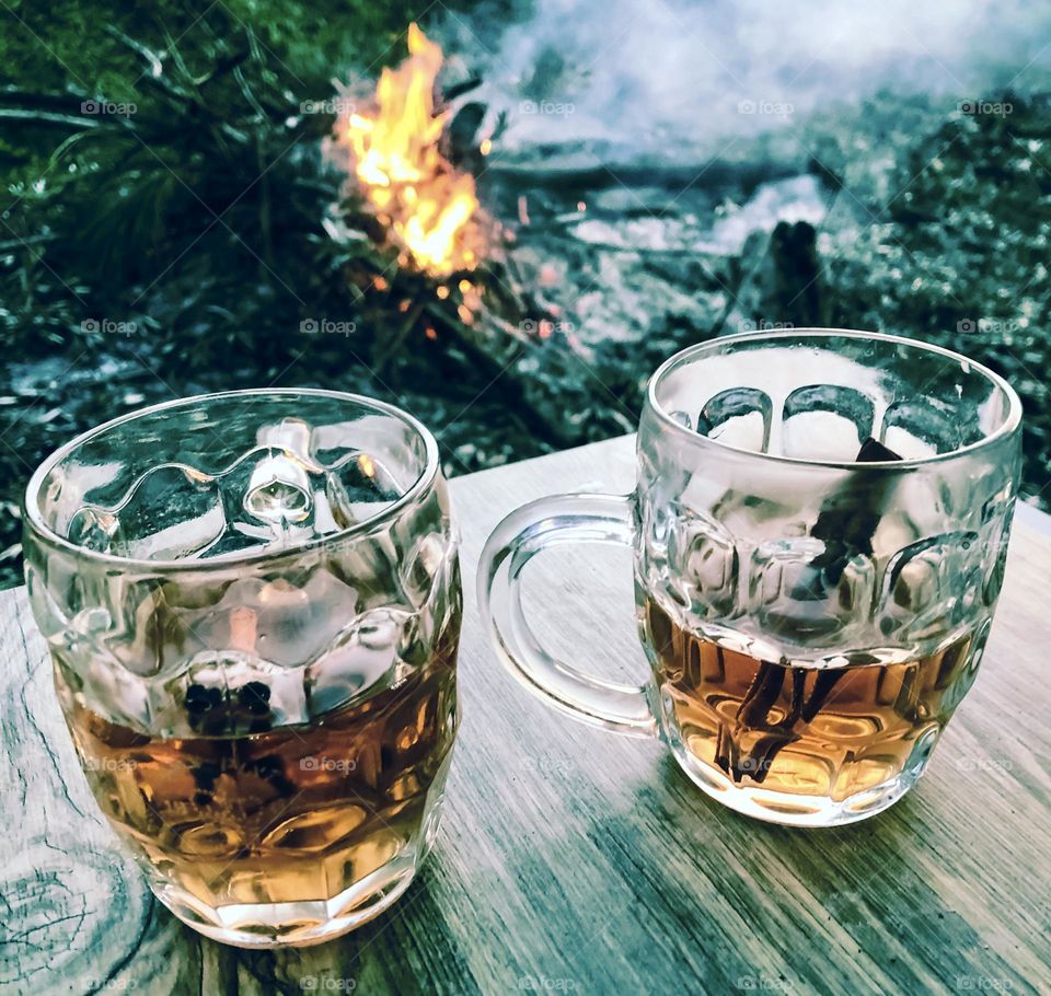 2 glasses of warming liquor with cinnamon on a table in front of a garden bonfire