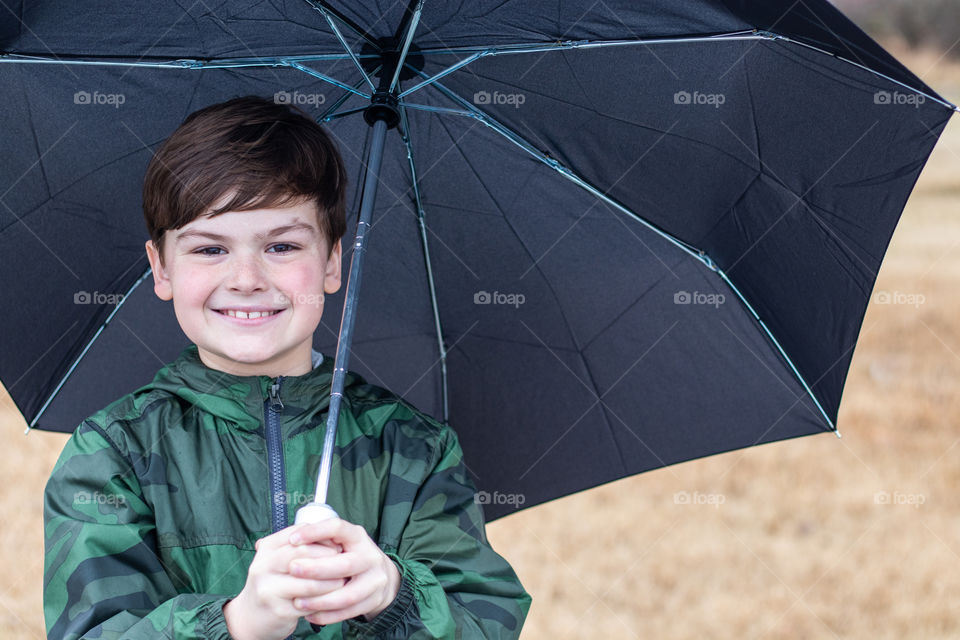 A boy in his raincoat holding an umbrella