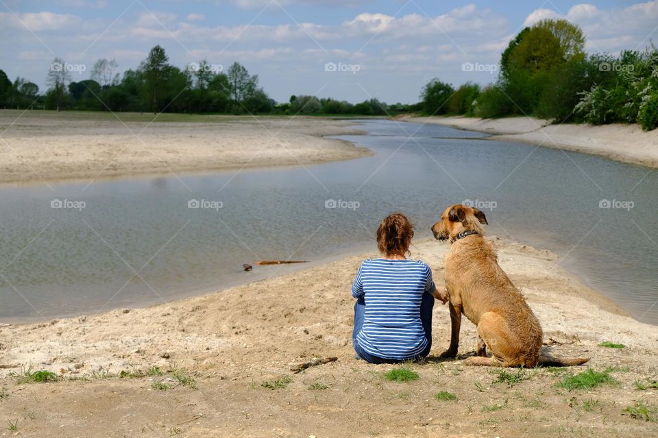 Rear view of woman and dog sitting by lake.