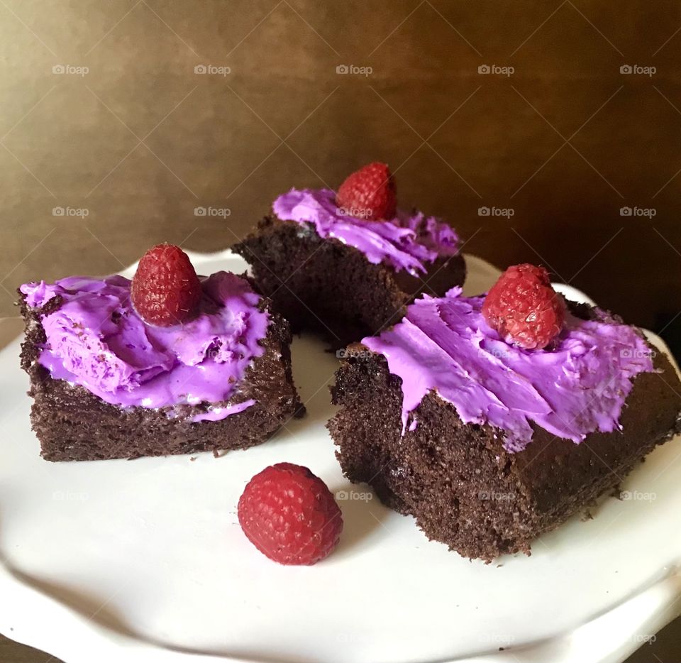 Sweet tooth craving - a delicious Serving of rich chocolate cake topped with bright purple creamy frosting with a yummy raspberry on top of each slice !  3 slices of deep dark chocolate cake. 
