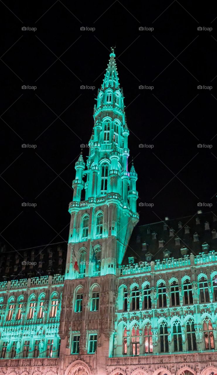 Beautiful view of the sharp spire of a medieval castle with gothic architecture and elements, illuminated with emerald light in the night city of Brussels on the Grand Place in Belgium, close-up side view.