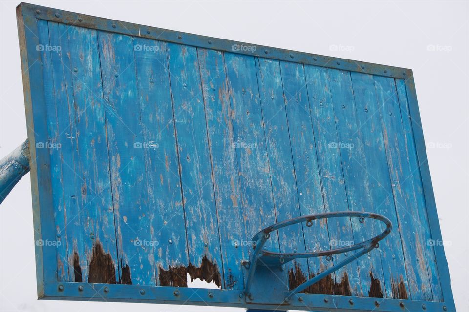 Closeup of a blue wooden outdoor basketball backboard, and rim.