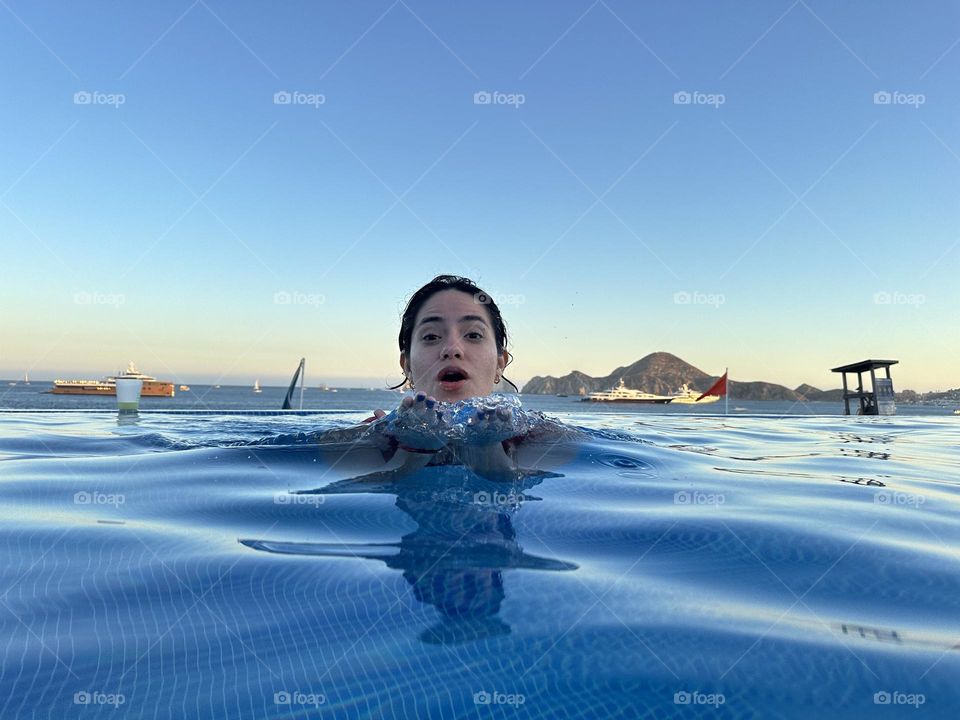 Portrait of a happy woman smiling and swimming in a pool with beautiful landscape as background.